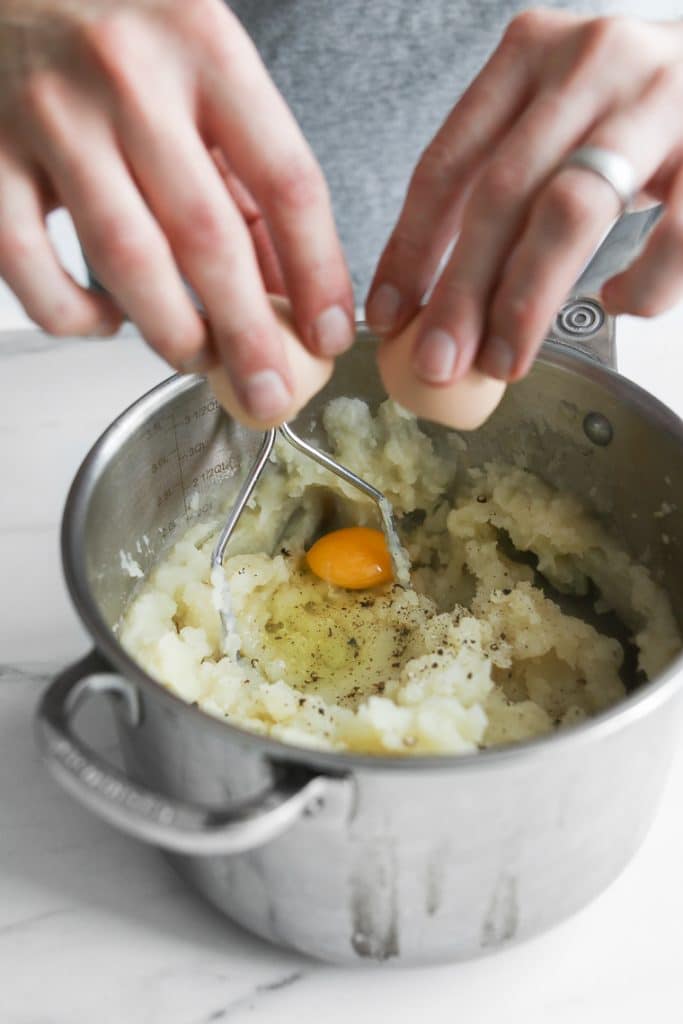 Phil's hands cracking an egg into mashed potatoes in a pot for the Beef Shepherd's Pie