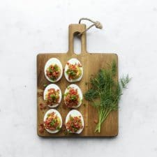 Six deviled eggs on a cutting board with a sprig of dill