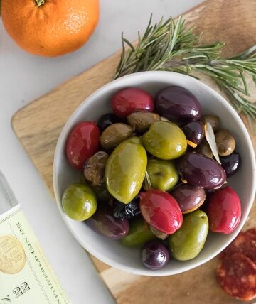 Colourful Warm Olives in a bowl, next to a bottle of gin laying on a marble table