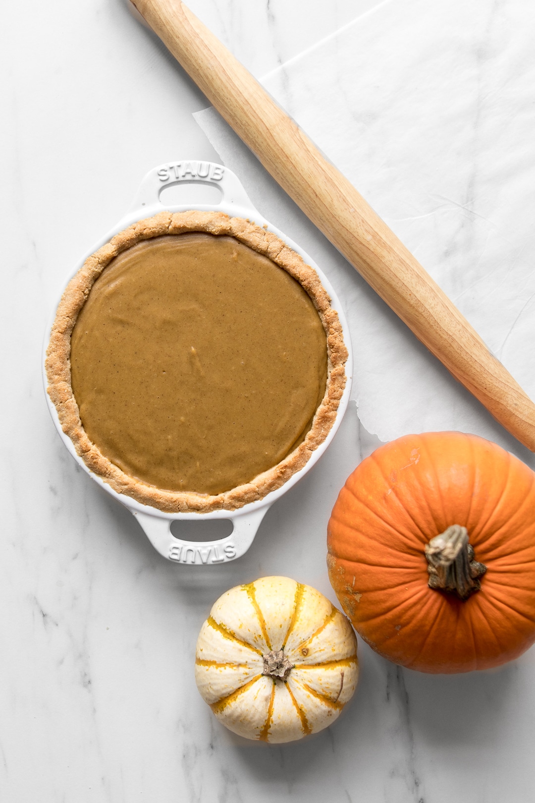 Whole30 pumpkin pie before baking with a rolling pin and two mini pumpkins