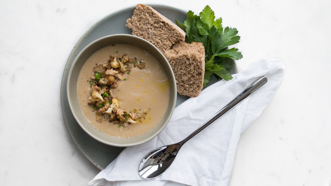 Cauliflower Soup on a plate with bread, a white napkin, and a spoon
