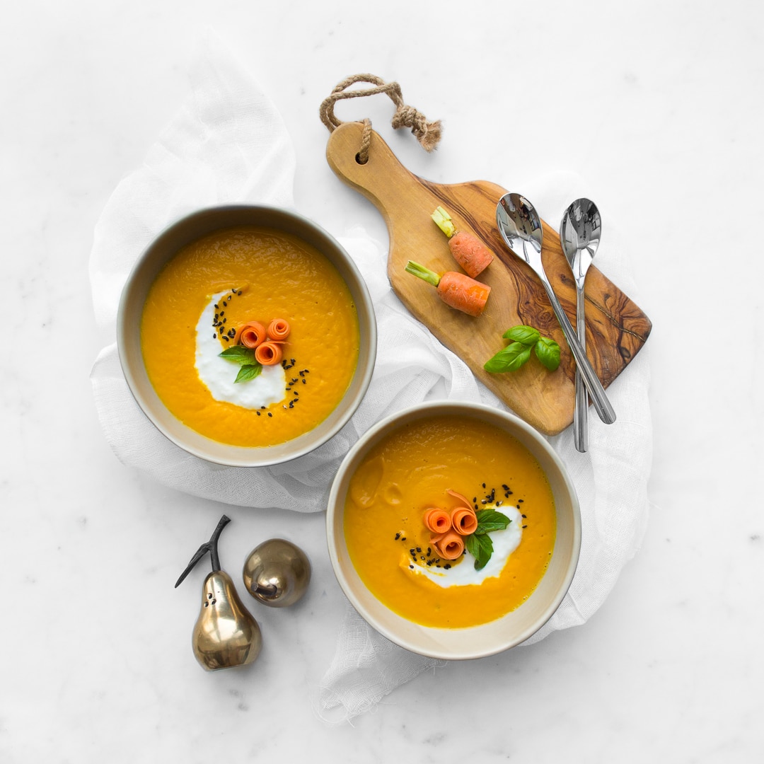 Two bowls of carrot and ginger soup styled with props