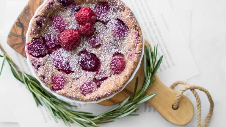 Raspberry Clafoutis on a wooden cutting board with sprig of rosemary