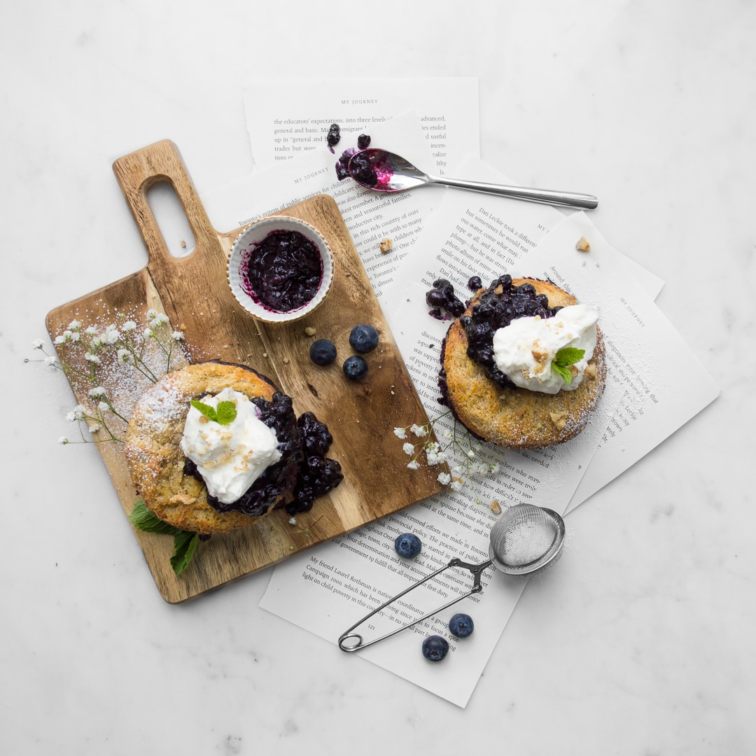 Flat lay of two mini Blueberry French Toast Cakes with whipped cream and blueberry sauce