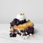 Side view of small Blueberry French Toast Cake topped with whipped cream and next to a sprig of baby's breadth