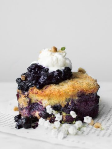 Side view of small Blueberry French Toast Cake topped with whipped cream and next to a sprig of baby's breadth