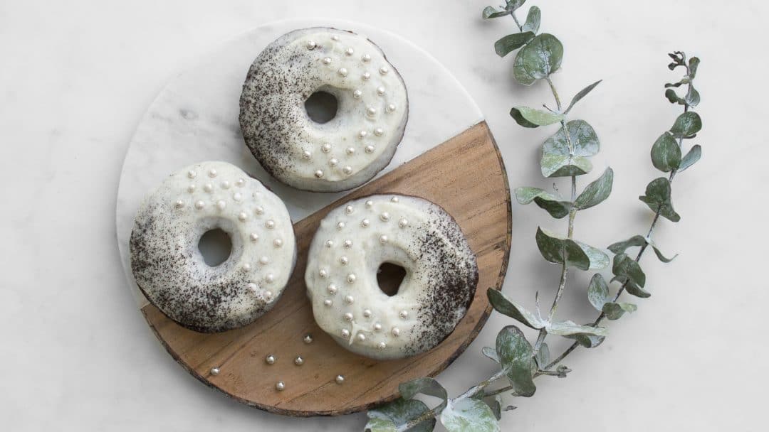 Three chocolate donuts with white frosting and silver balls on a wood and marble cutting board