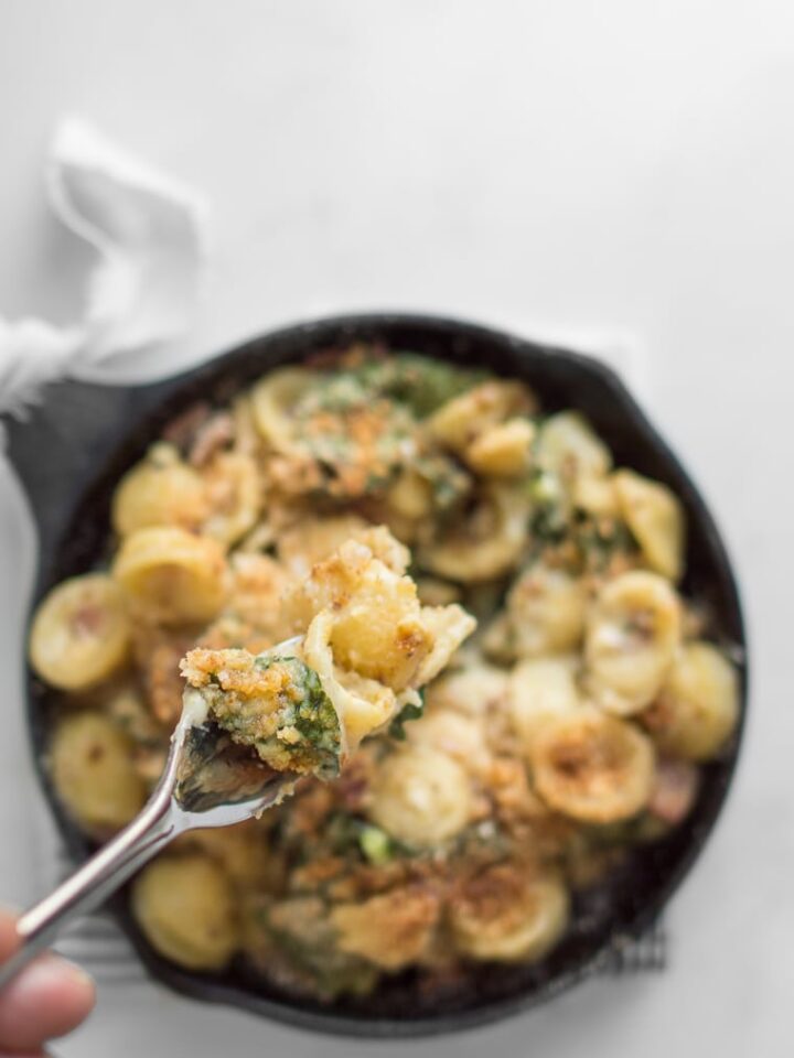 Fork full of camembert and kale mac and cheese above a skillet of mac and cheese