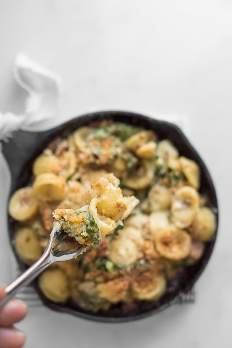 Fork full of camembert and kale mac and cheese above a skillet of mac and cheese