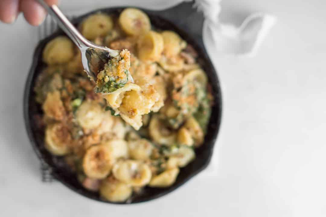 Overhead of fork with Kale Mac and Cheese with skillet of mac and cheese blurred in background