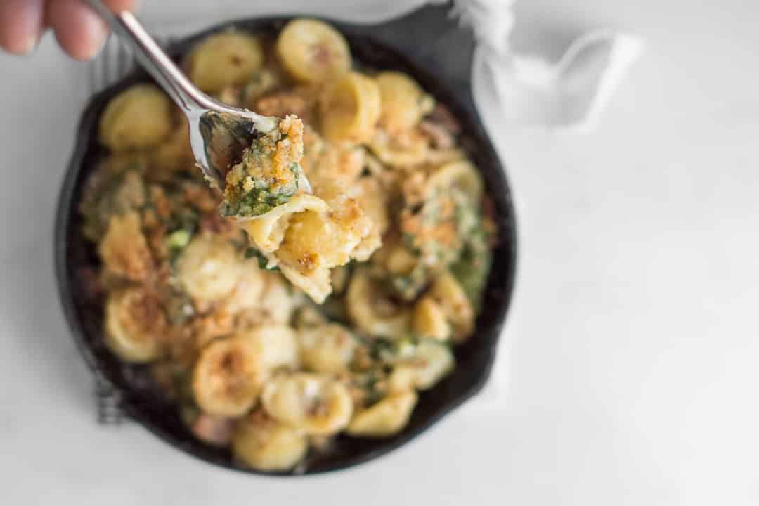 Overhead of fork with Camembert Mac and Cheese with skillet of mac and cheese blurred in background