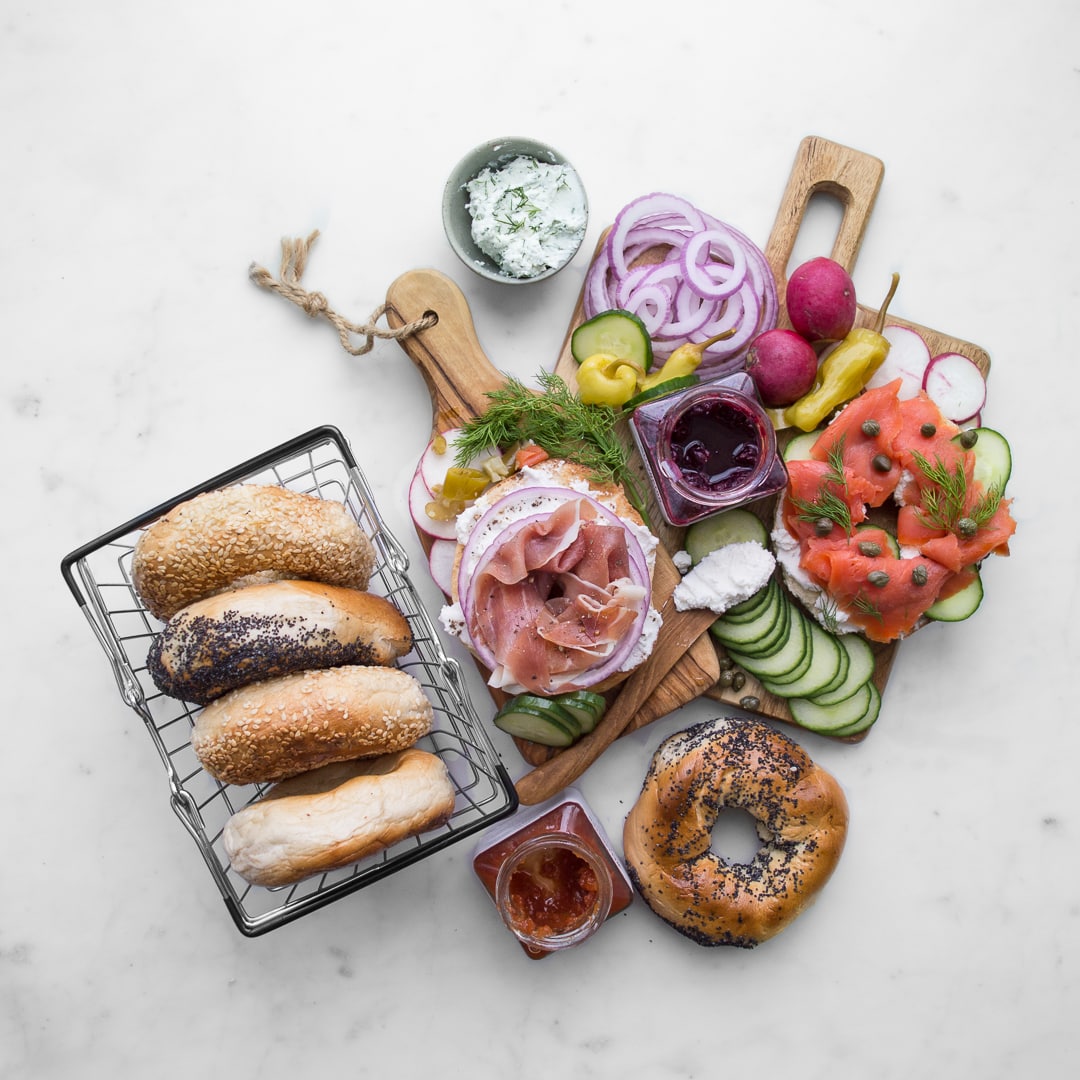 4 bagels in a basket and a wood board with bagel bar toppings