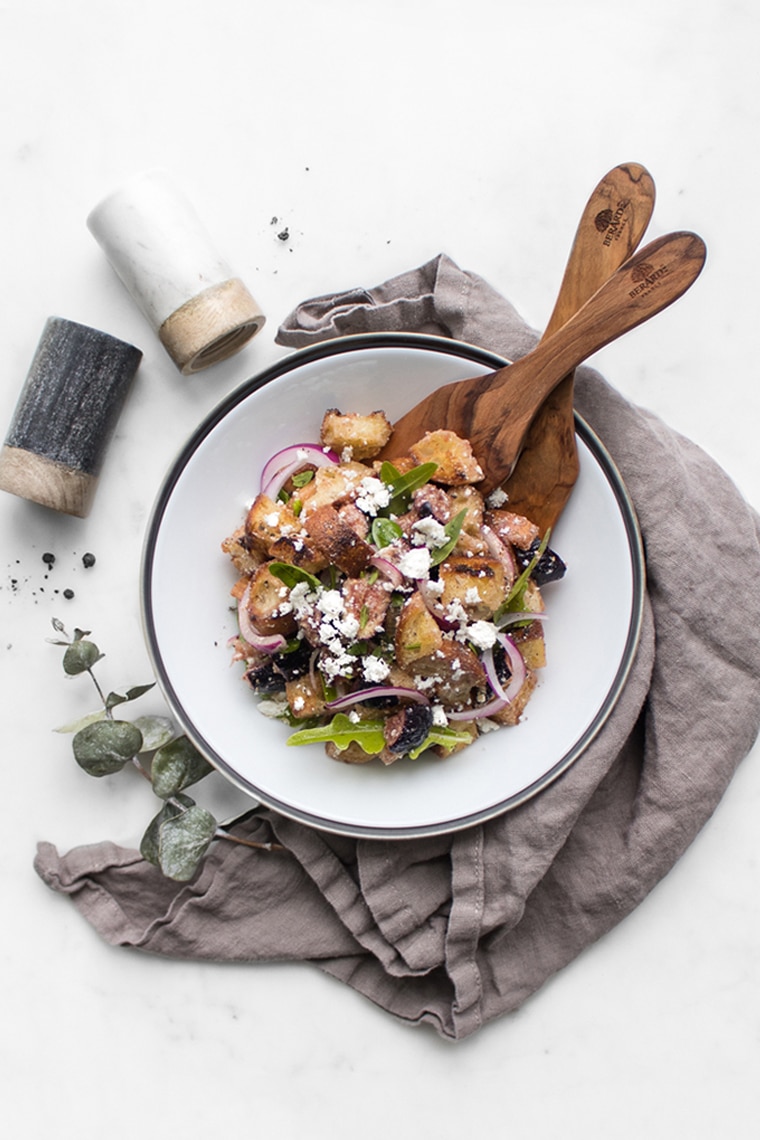 Fig Panzanella Salad in a bowl with tongs with napkin and salt and pepper shakers