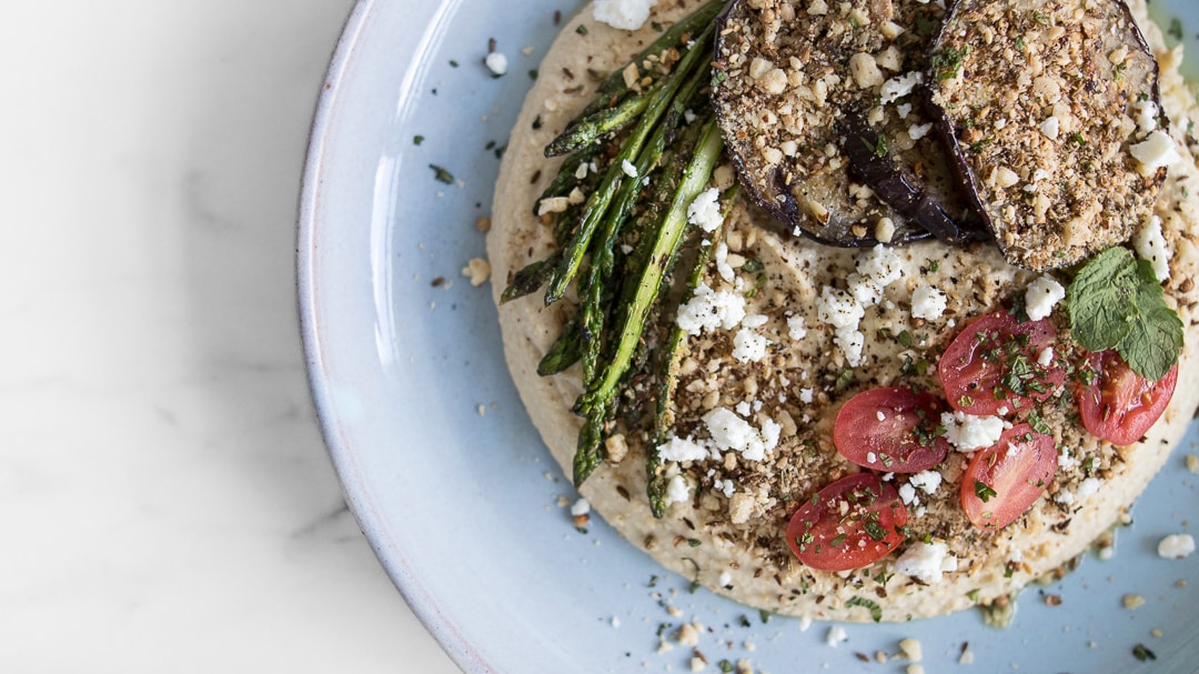 Close up of Hummus topped with Grilled Mediterranean Vegetables and Dukkah on a Blue Plate 