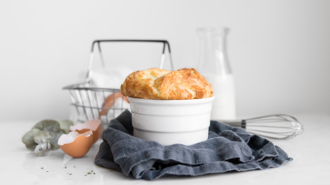 Cheese souffle on a blue napkin styled with egg shells, milk jar, and basket