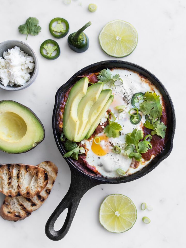 Close up of Mexican Shakshouka in a black skillet with sliced avocado