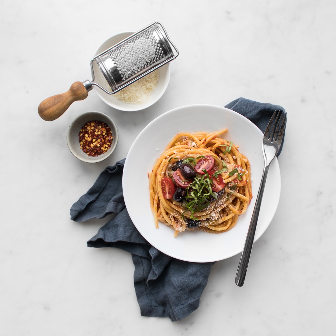 Flat lay of spaghetti puttanesca in a bowl with parmigiana reggiano and chili flakes