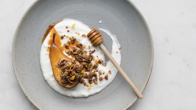 Roasted Pear with granola and yogurt on a grey plate with a honey stick