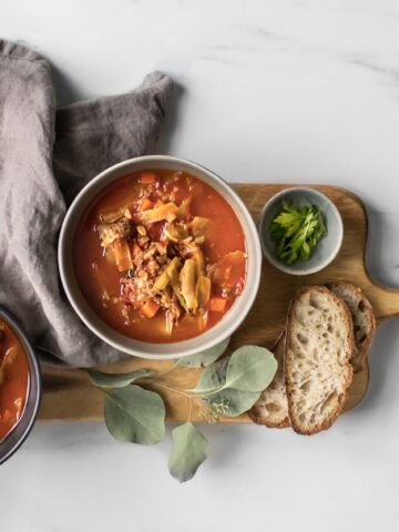 Overhead of two bowls of cabbage roll stew on a long wooden board with a napkin and slices of bread