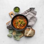 Overhead of black bowl of Cabbage Roll Stew on a wooden board with a grey napkin, diced bread, and small bowl of parsley