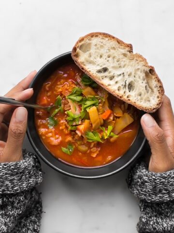 Mystique's hands holding a black bowl with Cabbage Roll Soup and a piece of bread.