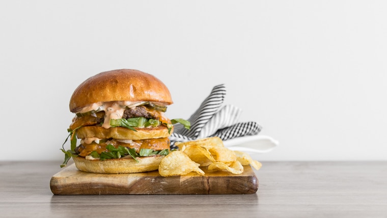 Image of the homemade big mac on a wood board with chips and napkin and lots of white space