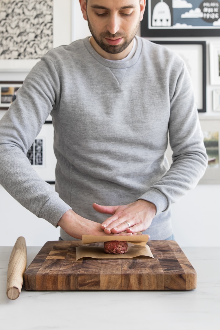 Male flattening out balls of ground beef in between two pieces of parchment paper