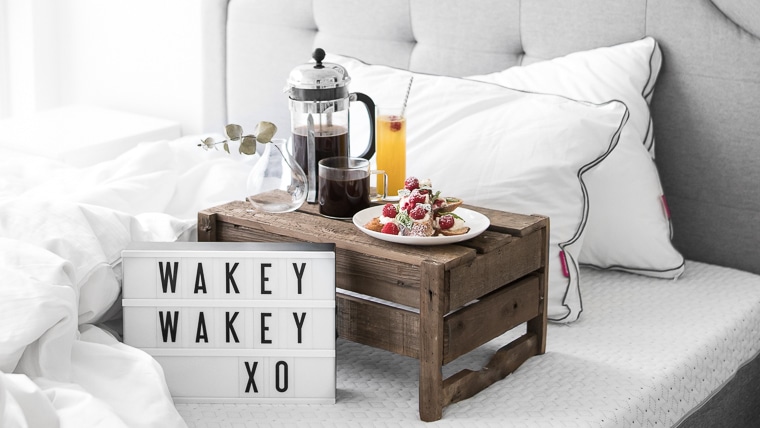 "Wakey Wakey XO" on small cinema sign laying on an Endy mattress with a cup of coffee, french toast, a newspaper, and two Endy pillows