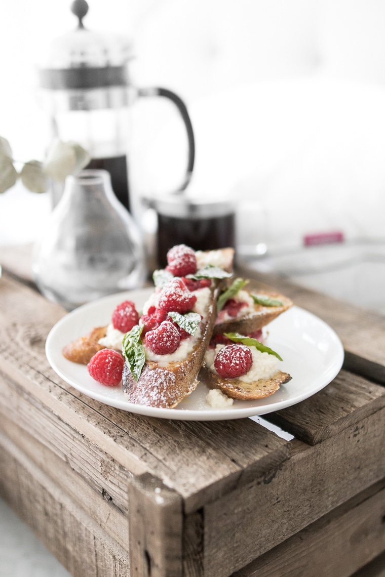 French toast with maple ricotta, raspberries and basil styled on a white plate on a wooden crate