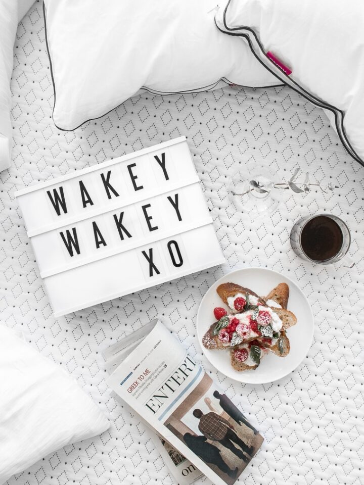 Overhead of "Wakey Wakey XO" on small cinema sign laying on an Endy mattress with a cup of coffee, french toast, a newspaper, and two Endy pillows