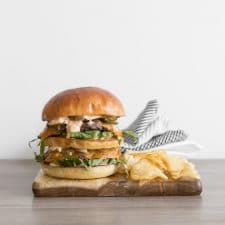 Close up image of a homemade big mac on a wood board with chips and a napkin