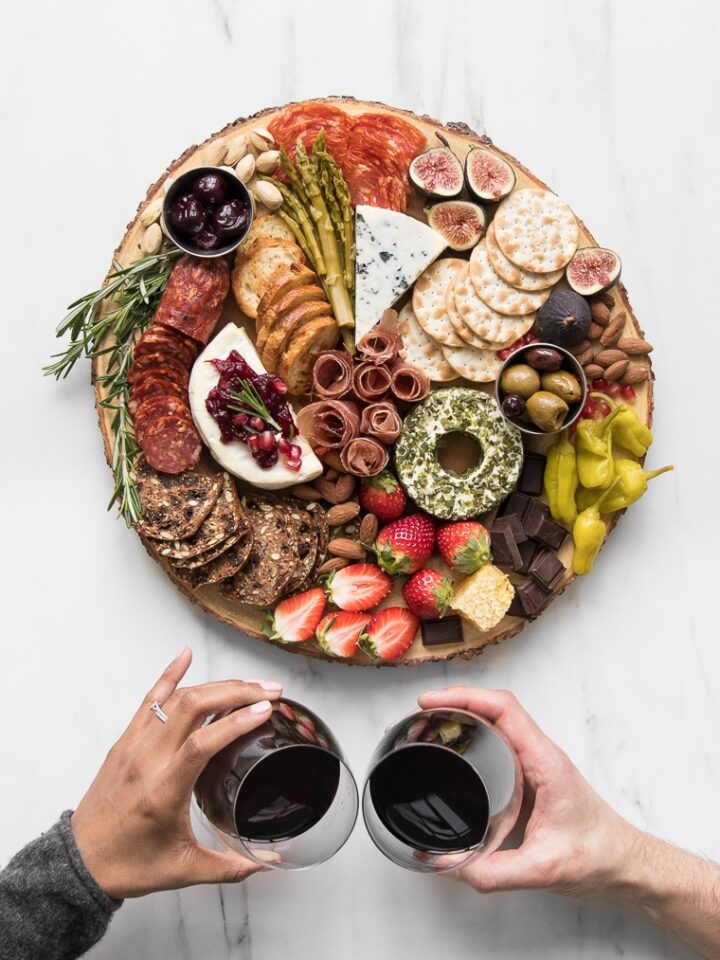 Philip and Mystique's hands holding wine and "cheersing" with a round styled cheeseboard on a marble table