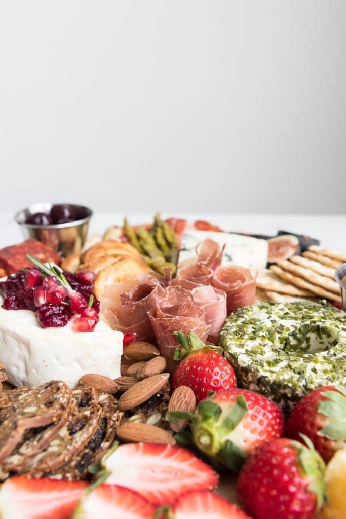 Cheese and Charcuterie Board with strawberries, crackers, nuts, prosciutto, and cranberries
