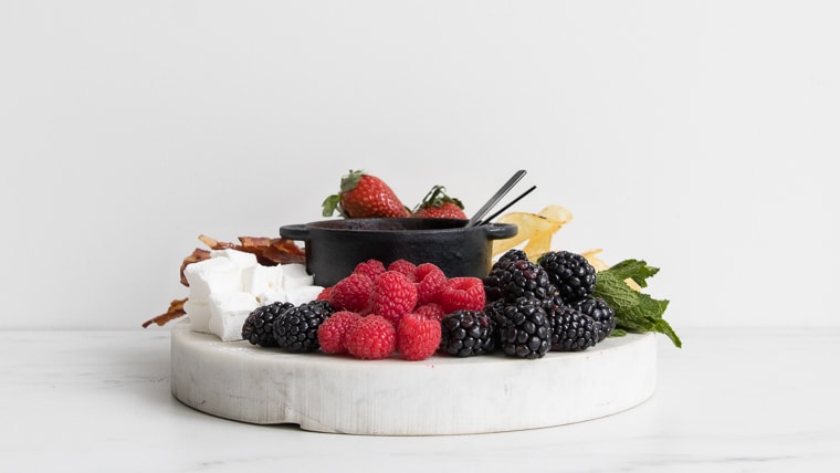Side view of marble slab with raspberries, blackberries and marshmallows, with a small cast iron pot with dark chocolate fondue for two
