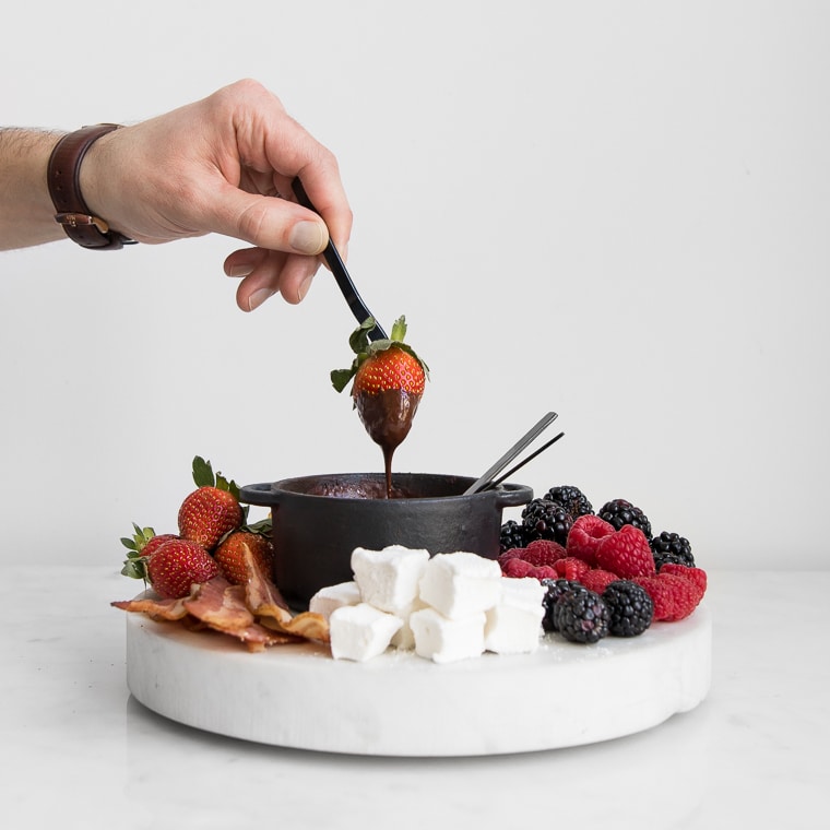 Philip's handing holding a fork with a strawberry dipped in dark chocolate fondue for two