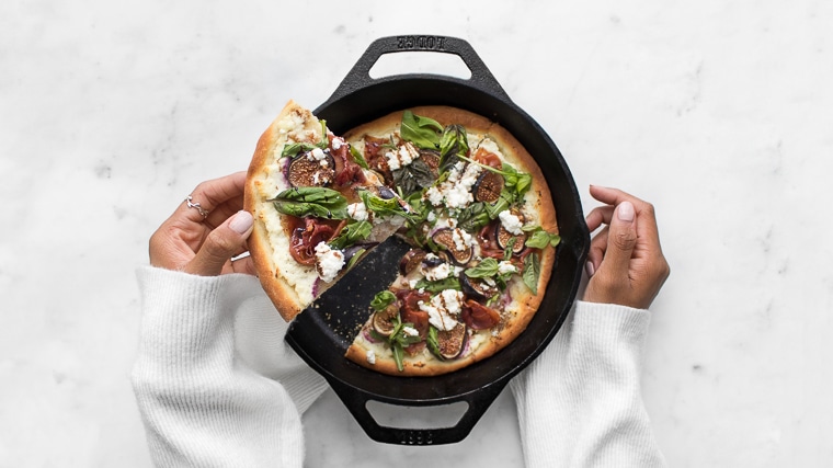 Mystique pulling out a piece of Fig and Prosciutto Pizza from a cast iron pan