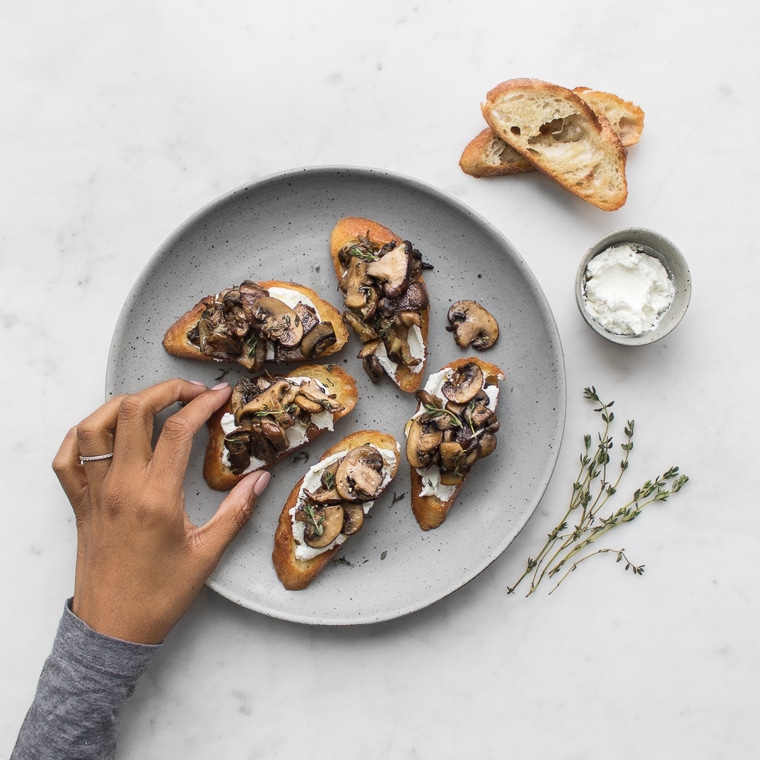 Mystique's Hand Grabbing a Piece of Mushroom Toast from a Grey Plate