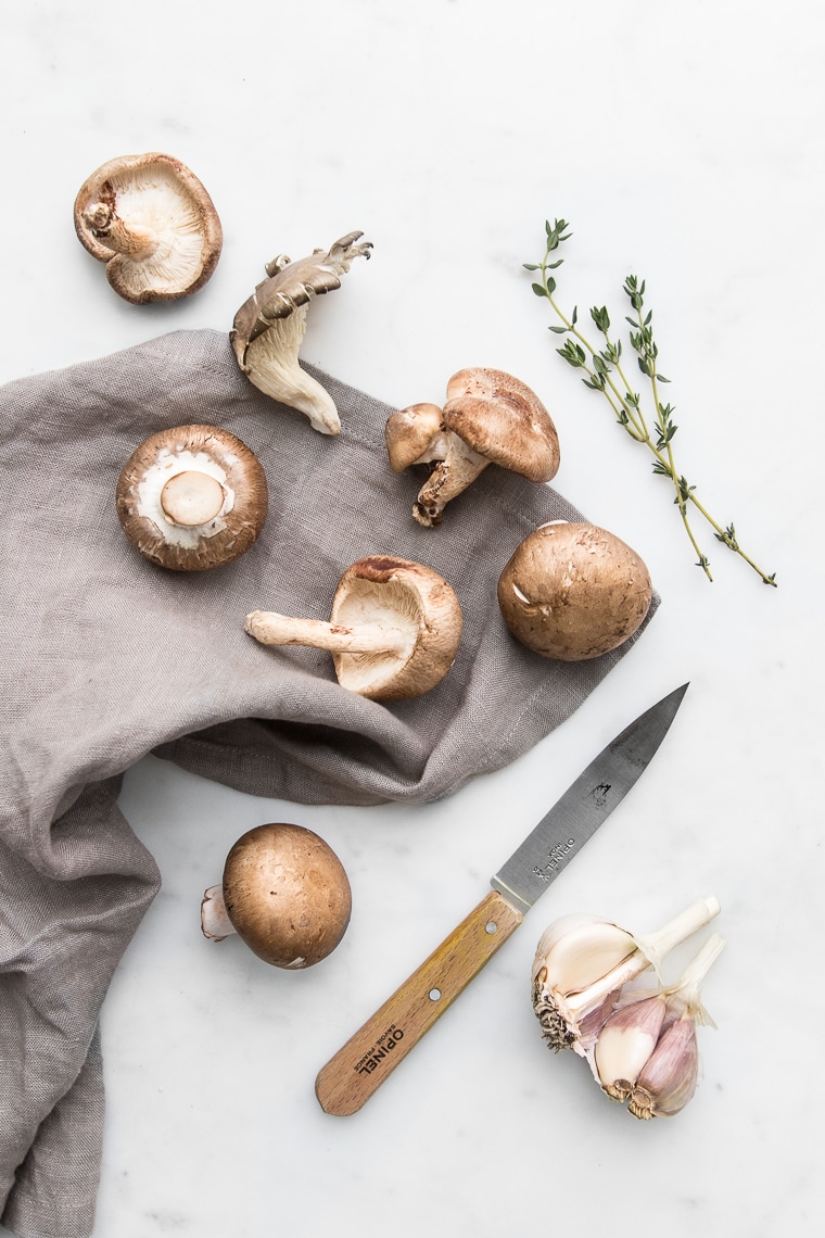 Mushrooms on a grey napkin with a pairing knife, thyme, and garlic