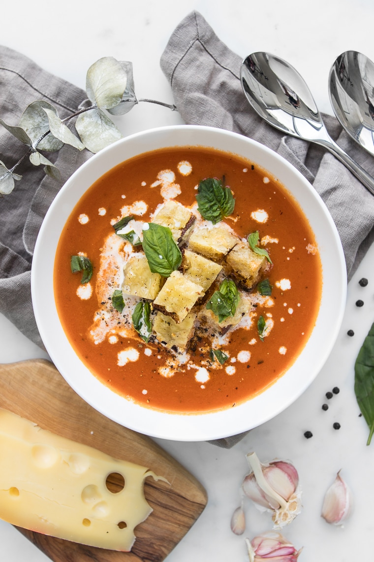 Close up of Roasted Tomato Soup next to a hunk of Jarlsberg Cheese