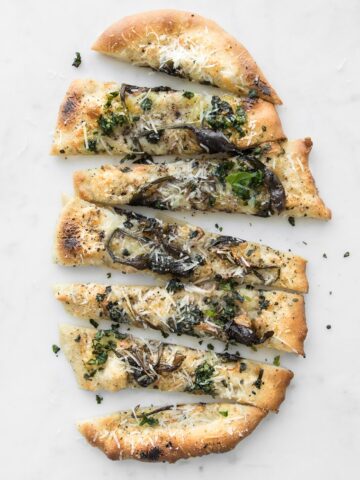 Sliced Cacio e Pepe Pizza with Spring Ramps on a white marble table