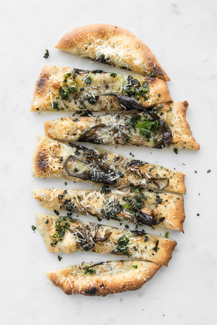 Sliced Cacio e Pepe Pizza with Spring Ramps on a white marble table