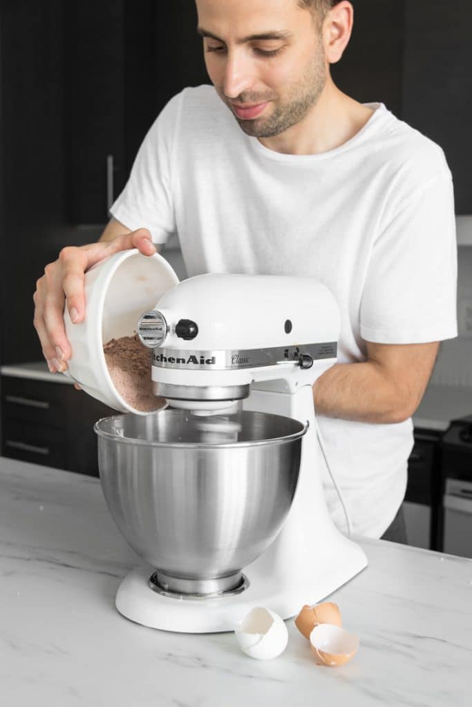 Guy in white shirt adding dry ingredients to Kitchen-Aid stand mixer