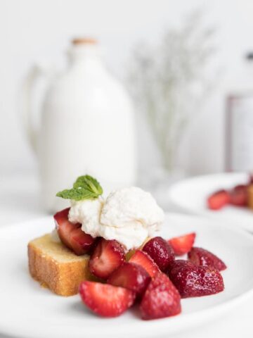 Side view of Strawberry Shortcake Cake with Mascarpone Cream and Strawberries with Maple Syrup Jug in Background