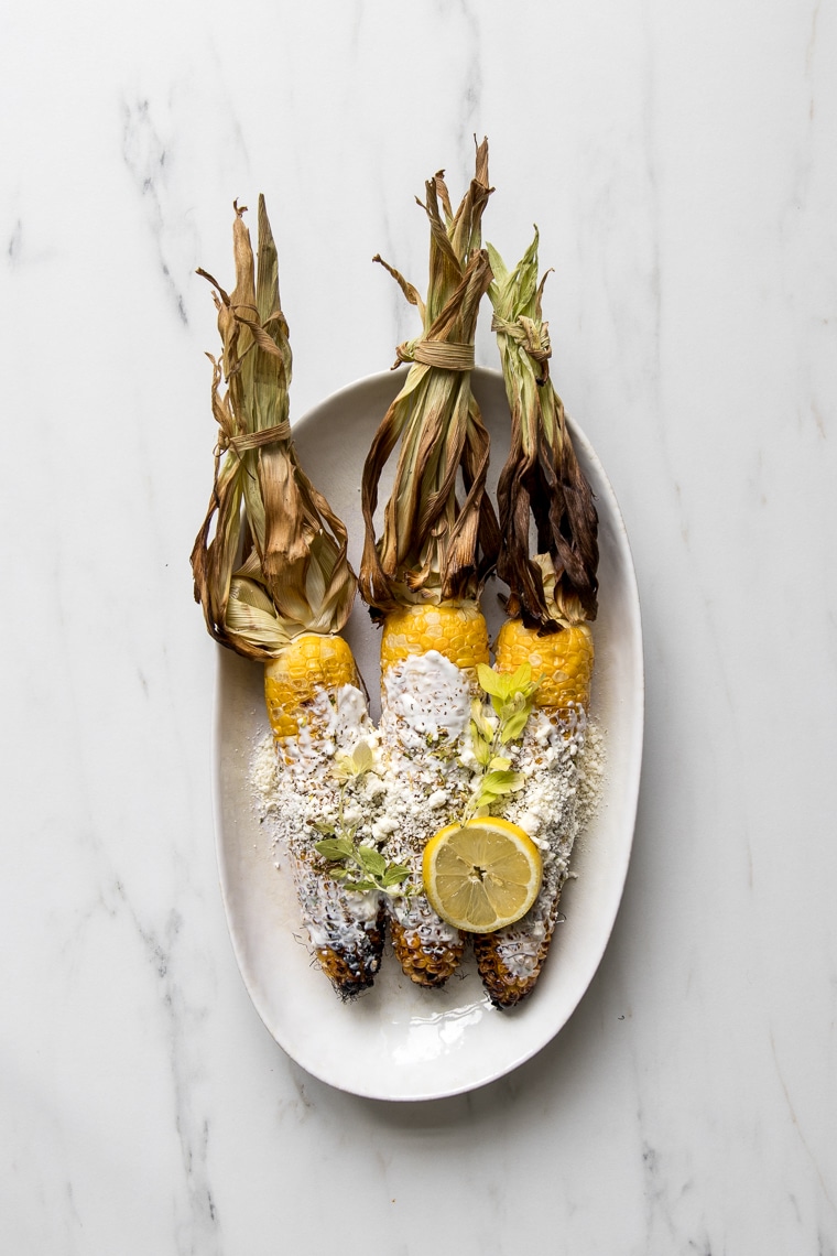 A plate with 3 grilled Greek street corn cobs