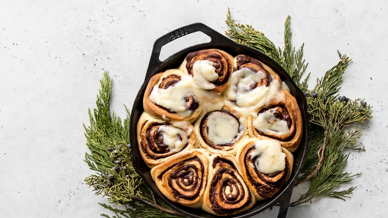 Chocolate rolls with cream cheese frosting in a skillet on top of cedar branches