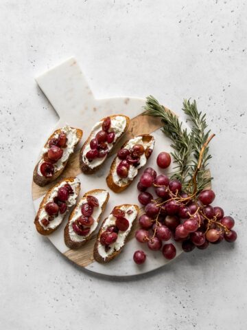 Grape and goat cheese crostini on a marble and wood board with grapes