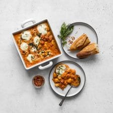 Baked gnocchi with vodka sauce being served with chunks of bread, basil, and chili flakes