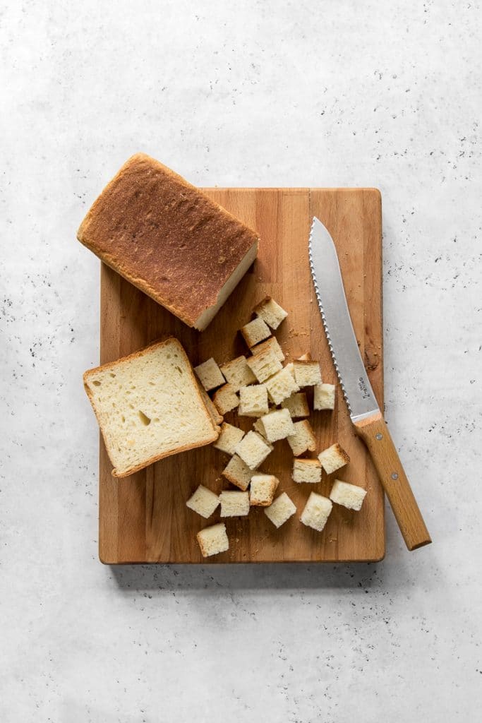 Loaf of bread on a cutting board being cut into cubes