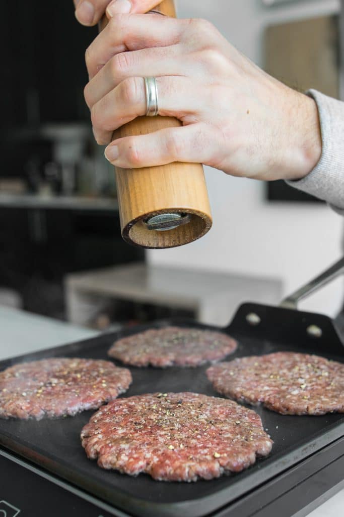 Seasoning hamburgers with pepper while they cook on a frying pan