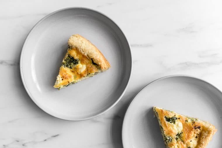 Two slices of broccoli and cheese quiche on grey plates